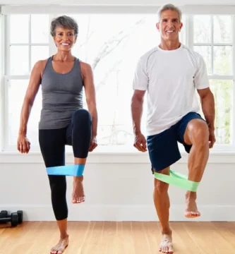 “Pareja de más de 50 años haciendo ejercicios suaves con bandas elásticas para fortalecer las articulaciones y mejorar la movilidad.”